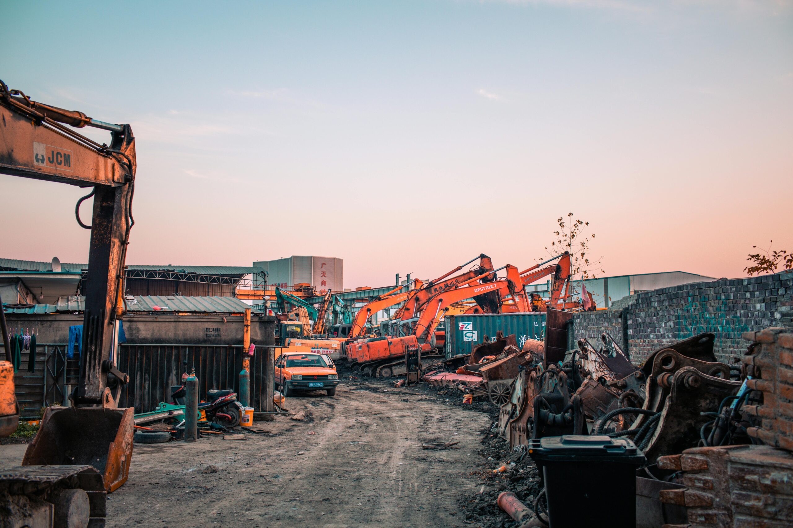 A busy construction site with industrial machinery at sunset, showcasing excavators and a vibrant sky.